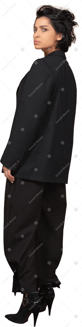 Vista posteriore di tre quarti di una donna d'affari scontenta in un abito nero, guardando la fotocamera
