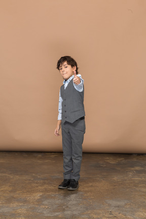 Vista frontal de um menino bonito de terno cinza, aparecendo o polegar