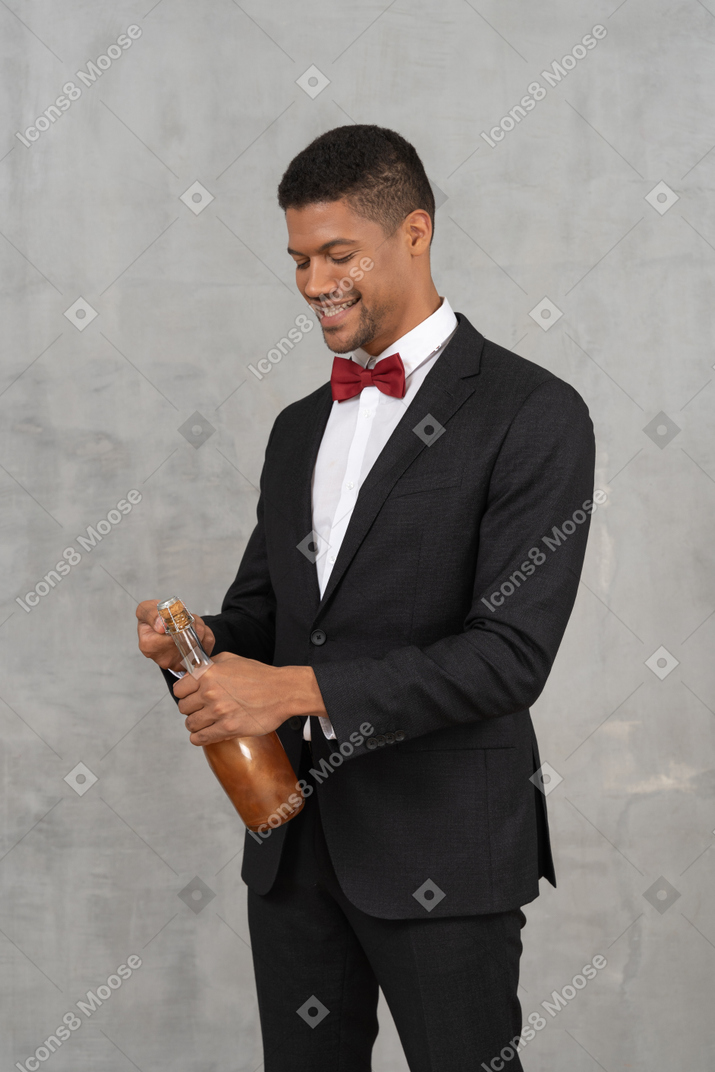 Smiling young man opening a bottle of champagne