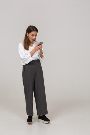Vista di tre quarti di una giovane donna in abiti da ufficio che controlla l'alimentazione tramite telefono