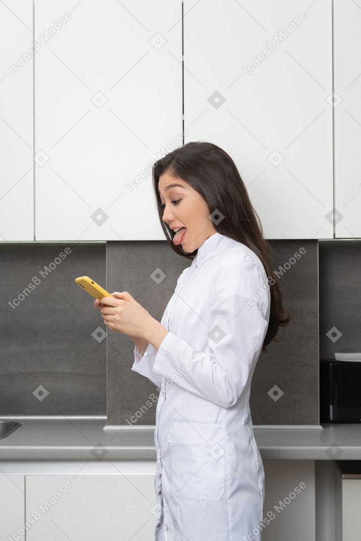 Side view of a female doctor chatting via her phone and putting out her tongue