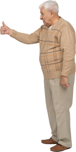 Vue latérale d'un vieil homme heureux dans des vêtements décontractés montrant le pouce vers le haut