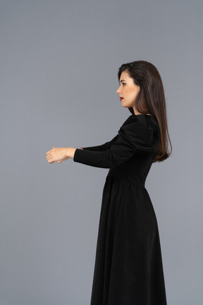 Vista laterale di una giovane donna in un abito nero che tende le mani