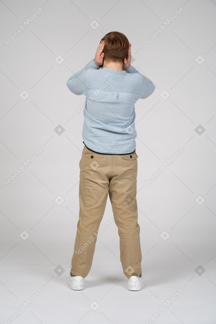 Vista traseira de um menino cobrindo os ouvidos com as mãos