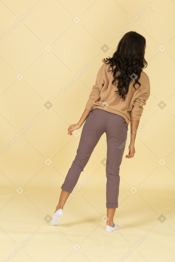 Back view of a curious dark-skinned young lady leaning on her leg