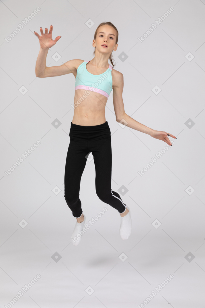 Vorderansicht eines jugendlich mädchens in der sportbekleidung, die hand beim springen ausstreckt