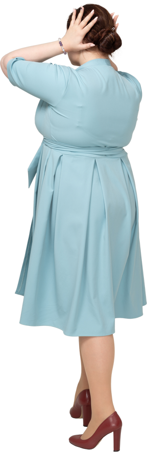 Вид сзади женщины в синем платье, касающейся ее волос