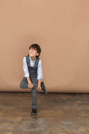 Front view of a boy in suit standing on one leg and making faces