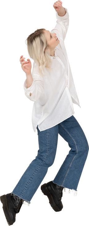 Vue de trois quarts d'une femme blonde en vêtements décontractés dansant sur la pointe des pieds et en levant les mains et la tête