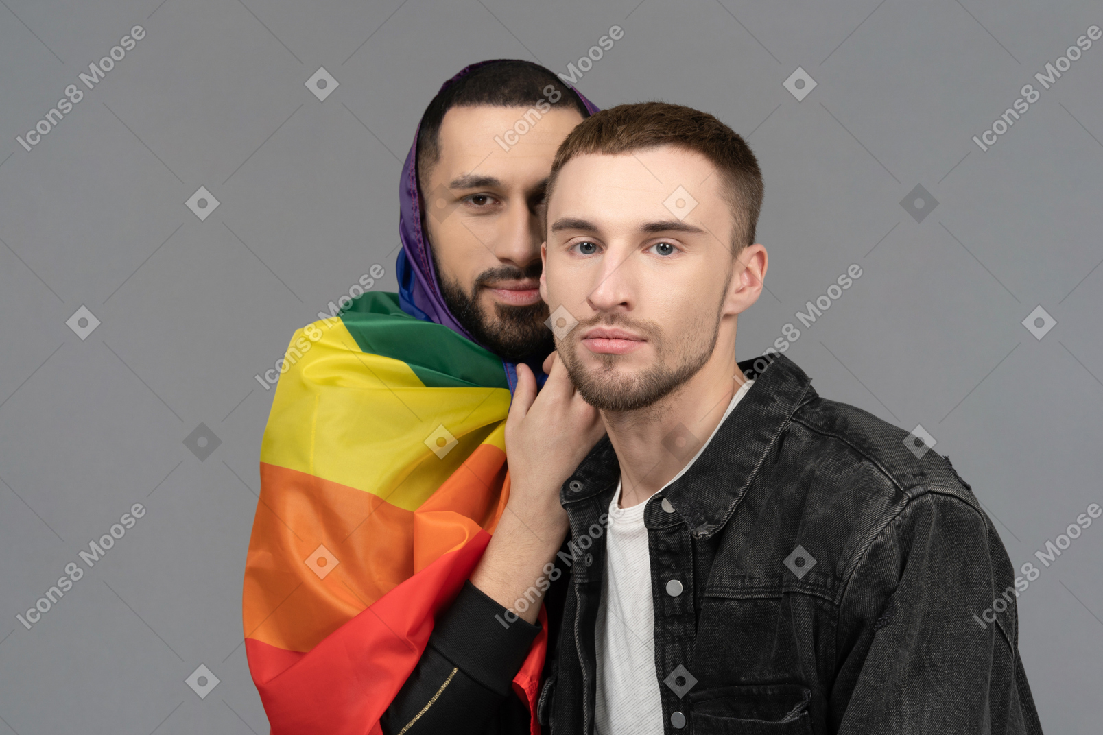 Close-up of young man wrapped in lgbt flag standing behind another young man