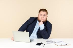 Pensativo joven trabajador de oficina con sobrepeso sentado en el escritorio de oficina