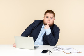 Pensive young overweight office worker sitting at office desk