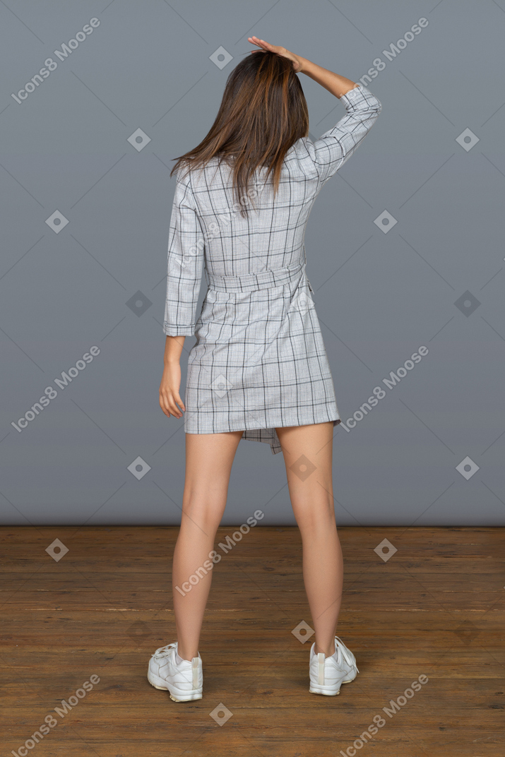 Unrecognizable slim young woman standing back to camera keeping one hand on her head