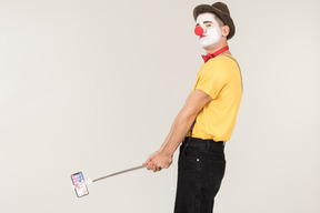Male clown holding phone on selfie stick