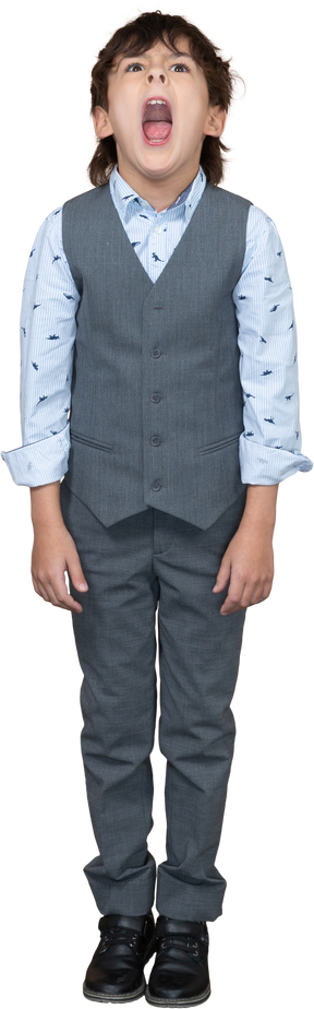 Vista frontal de un niño con traje gris de pie con la boca abierta y mirando hacia arriba