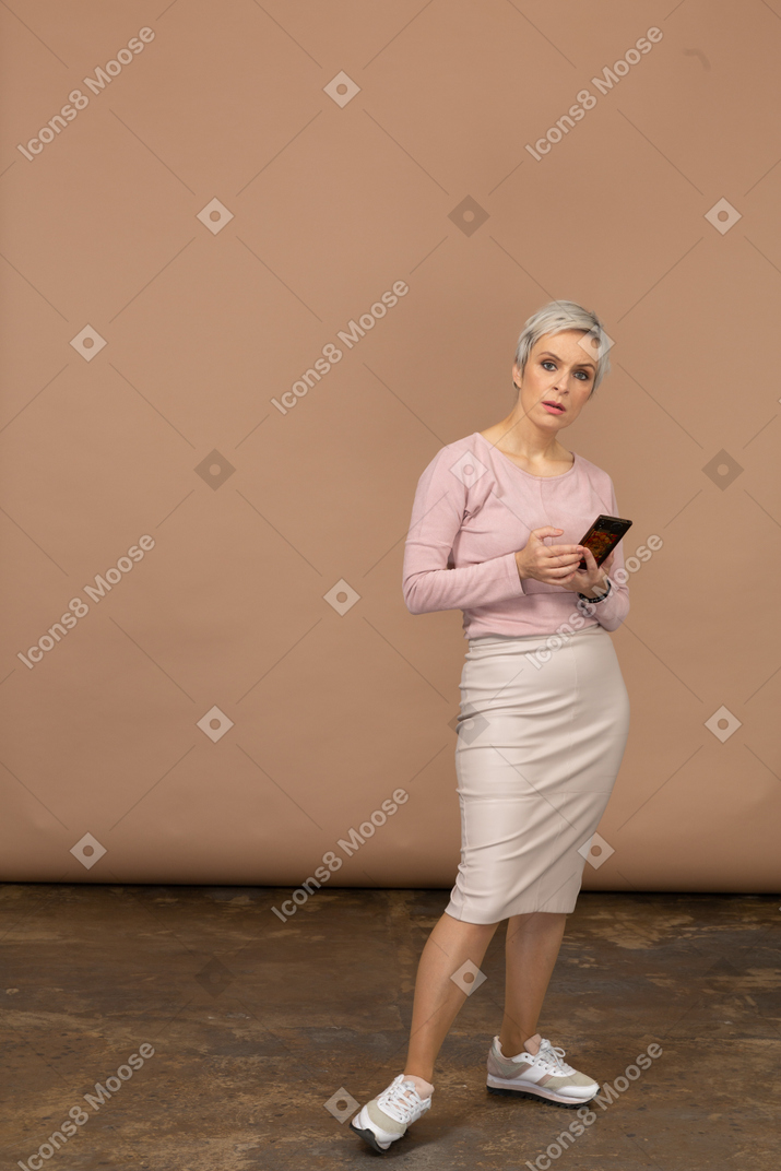Front view of a woman in casual clothes holding phone and looking at camera