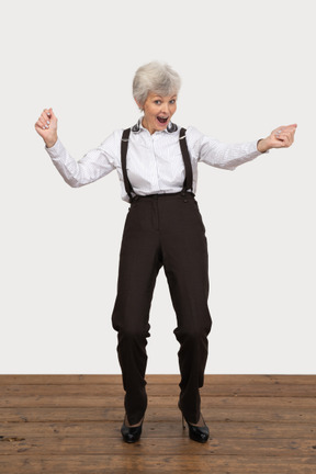 Вид спереди счастливой старушки в офисной одежде, поднимающей руки во время крика