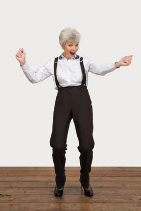 Front view of a happy old lady in office clothing raising hands while screaming