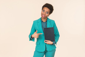 Jeune femme noire avec une coupe de cheveux courte, posant dans un costume bleu avec un comprimé à la main