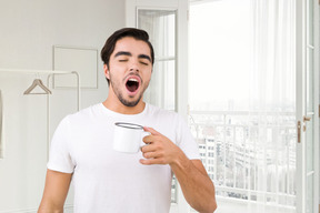 A man holding a cup of coffee and yawning
