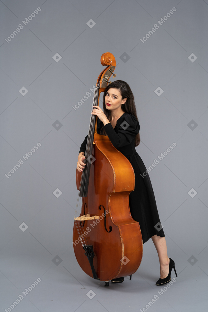 Vista di tre quarti di una giovane musicista in abito nero che tiene il suo contrabbasso