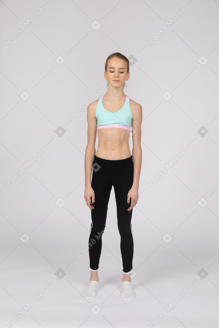 Front view of a teen girl in sportswear standing still and looking down