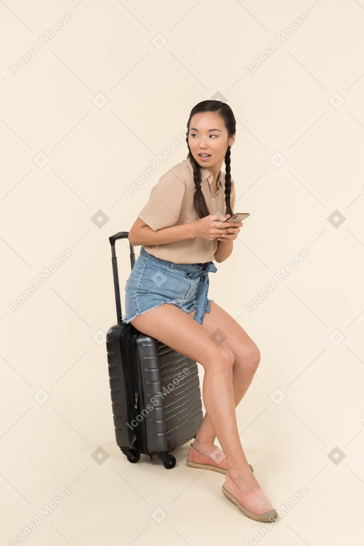 Young female traveller holding phone and sitting on the phone