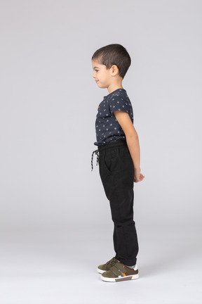 Вид сбоку застенчивого мальчика в повседневной одежде, стоящего с руками за спиной и смотрящего вниз