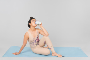 Joven gimnasta indio sentado en la estera de yoga y tomando café