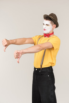Sad looking male clown standing half sideways and showing thumbs down with both hands