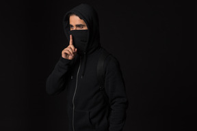 Hacker guy standing in the dark and showing silence gesture