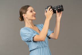 Vista de tres cuartos de una mujer joven sonriente en vestido azul tomando tiro