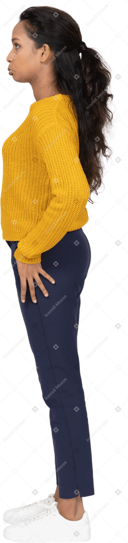 Vista lateral de una niña en ropa casual de pie con la mano en la cadera y haciendo muecas