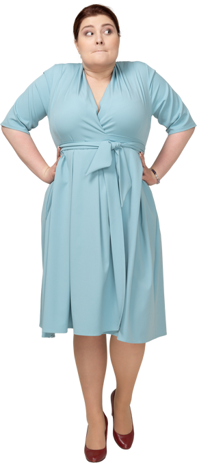 Vista frontal de uma mulher de vestido azul em pé com as mãos na cintura e fazendo caretas
