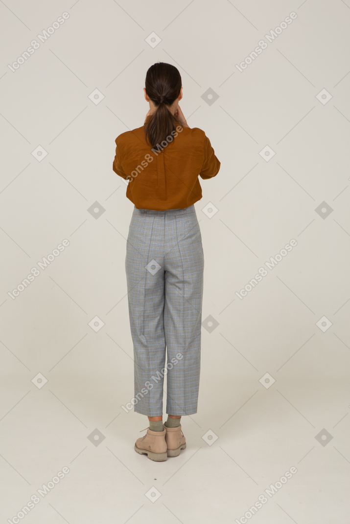 Vista traseira de uma jovem mulher asiática de calça e blusa tocando seu rosto