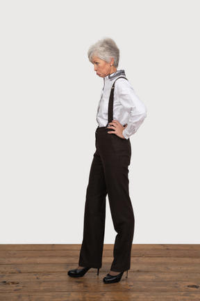 Vista lateral de una anciana disgustada en ropa de oficina poniendo las manos en las caderas