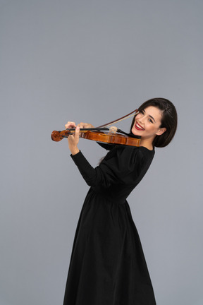 Close-up de uma jovem alegre de vestido preto tocando violino