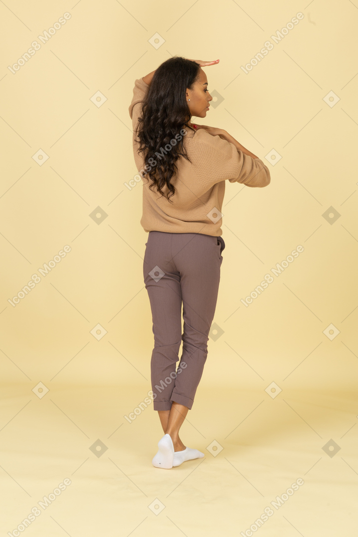 Three-quarter back view of a dark-skinned young female holding hands horizontally near her face