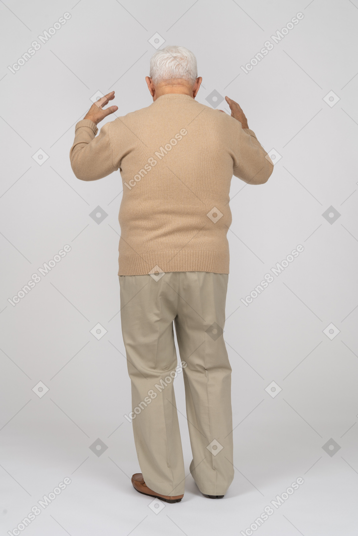 Rear view of an old man in casual clothes standing with raised hands