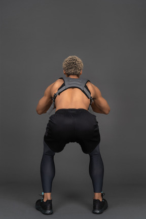 Vista posteriore di un uomo afro accovacciato a torso nudo