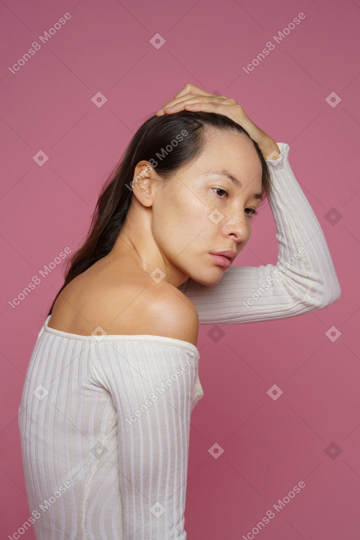 Vue de trois quarts d'une triste femme aux cheveux noirs touchant ses cheveux et regardant de côté