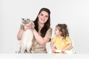Mutter sitzt neben einer tochter im kinderstuhl und hält eine katze