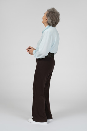 Vista laterale di una donna anziana che osserva in su con le mani giunte