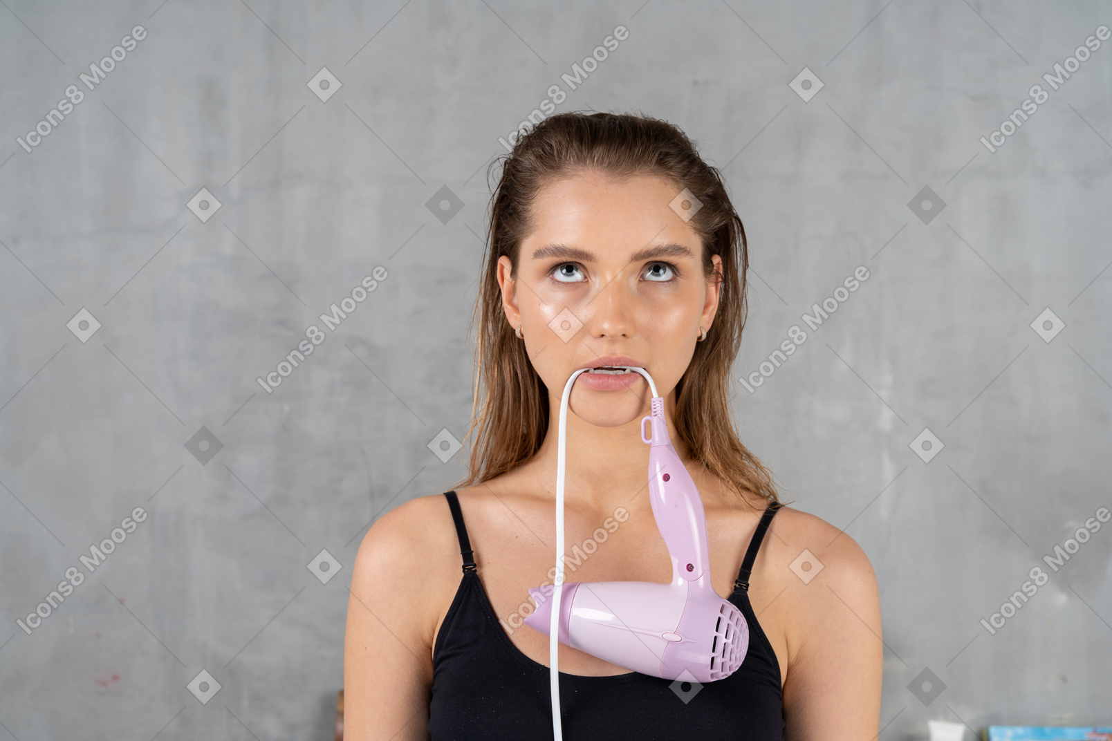 Front view of a young woman biting a hairdryer cord while looking fed up
