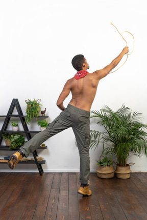 Back view of muscular man standing on one leg and lassoing