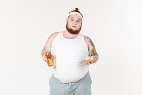 Ein dicker mann in sportkleidung mit einer flasche bier und einer handvoll pommes