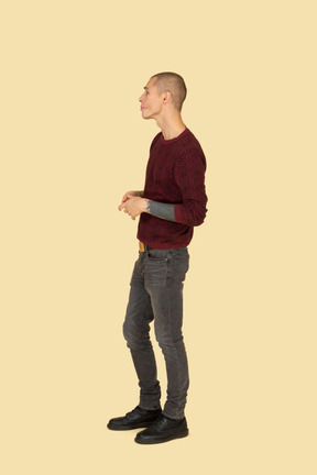 Side view of a pouting young man in casual clothes holding hands together