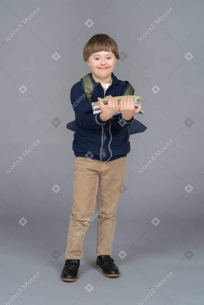 Cheerful little boy with a backpack holding books