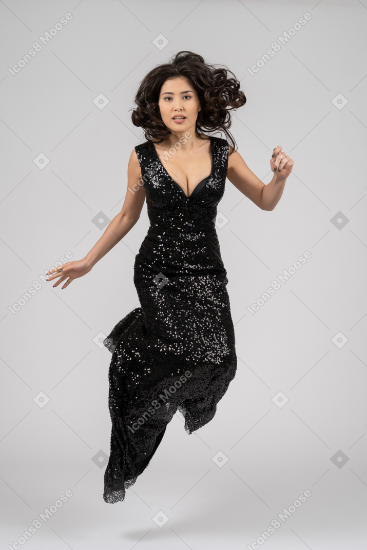 Красивая женщина в черном вечернем платье прыгает