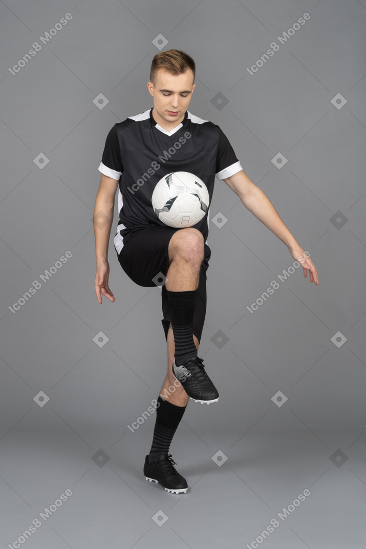 Three-quarter view of a male football player raising leg and kicking a ball